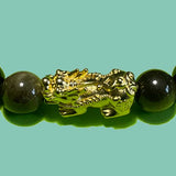 Zoom sur le PIXIU du Bracelet en perles d'obsidienne noir dorée avec un fond légèrement vert.