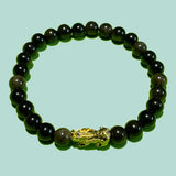Bracelet en perles d'obsidienne noir dorée avec un fond légèrement vert. Une petite figurine représentant un PIXUI  fait partir du bracelet.